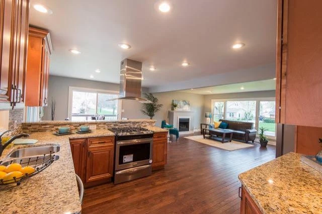 An open-concept kitchen with wood cabinets, granite countertops, and stainless steel appliances connected to a living room